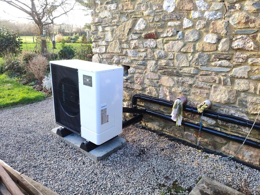Mitsubishi Electric Ecodan outdoor air source heat pump installed on a concrete base beside a stone wall